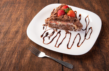 Chocolate cake, a tasty slice of chocolate cake with strawberries on a white plate on rustic wood, abstract background, selective focus.