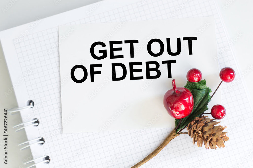 Poster text get out of debt on a white card that lies on a notebook on the table next to a decorative branc
