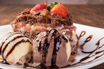 Chocolate cake, a tasty slice of chocolate cake with strawberries and ice cream balls on a white plate on rustic wood, abstract background, selective focus.