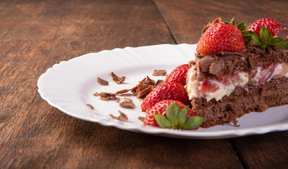 Chocolate cake, a tasty slice of chocolate cake with strawberries on a white plate on rustic wood, abstract background, selective focus.