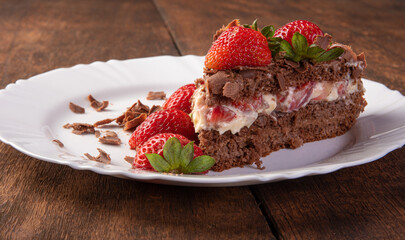 Chocolate cake, a tasty slice of chocolate cake with strawberries on a white plate on rustic wood, abstract background, selective focus.