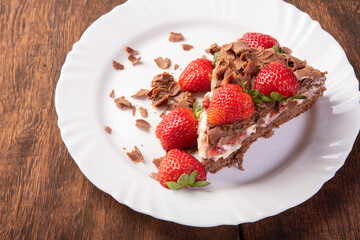Chocolate cake, a tasty slice of chocolate cake with strawberries on a white plate on rustic wood, abstract background, selective focus.