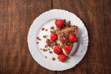 Chocolate cake, a tasty slice of chocolate cake with strawberries on a white plate on rustic wood, abstract background, Top view.