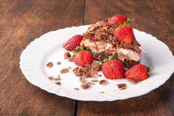 Chocolate cake, a tasty slice of chocolate cake with strawberries on a white plate on rustic wood, abstract background, selective focus.