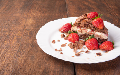 Chocolate cake, a tasty slice of chocolate cake with strawberries on a white plate on rustic wood, abstract background, selective focus.