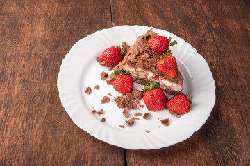 Chocolate cake, a tasty slice of chocolate cake with strawberries on a white plate on rustic wood, abstract background, selective focus.