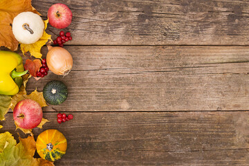 Pumpkins, apples, onions and peppers with autumn leaves lie on a wooden background