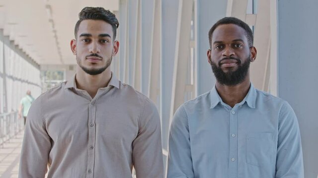Portrait two serious men multiracial business partners coworkers businessmen african american guy manager and hispanic man investor standing indoors in office posing in corridor looking at camera