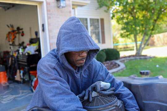 A Portrait Of A Black African-American Man Fixing A Lawnmower