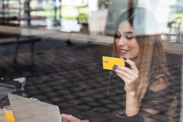 Smiling woman holding credit card for online shopping while making orders at coffee shop. Business, lifestyle, technology, ecommerce, digital banking and online payment concept