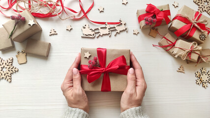 Woman's hands hold christmas holiday present in craft paper with red ribbon.