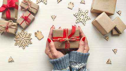 Woman's hands hold christmas holiday present in craft paper with red ribbon and jute rope.