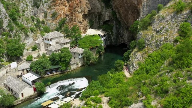 Aerial: Beautiful Shot Of Buna River Amidst Structures At Vrelo Bune, Drone Flying Over Green Forest During Sunny Day - Blagaj, Bosnia and Herzegovina