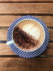 Delicious cappuccino cup on wooden background. Blue and white crockery, hipster vibes. Top view. Coffee with chocolate powder