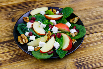 Autumn spinach salad with apple, feta cheese, walnut and dried cranberry on wooden table. Healthy vegetarian food