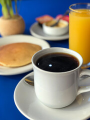 cup of coffee in the background out of focus hot cakes and orange juice, on table with blue fabric. breakfast