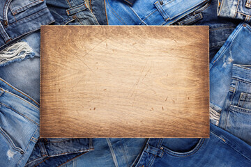 Stack of blue jeans denim and wood name plate. Jeans heap with wooden background texture