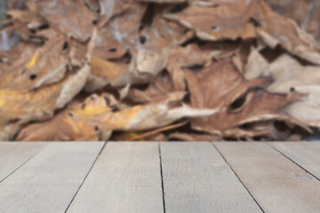 Empty wooden table mockup in front of a large pile of brown fall leaves background.