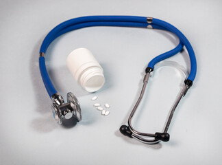 Stethoscope and jar of white pills on blue gray background. Medical and cardio heart health concept.