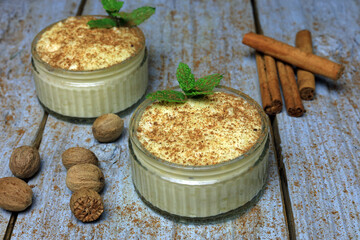 ground nutmeg and cinnamon sprinkled over thick clotted cream rice pudding served in a glass bowl.