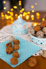 Homemade chocolate candy truffles sprinkling with cocoa, coconut chips and cookie crumbs on the table laid for Christmas or New Year with blue candlesticks and garland