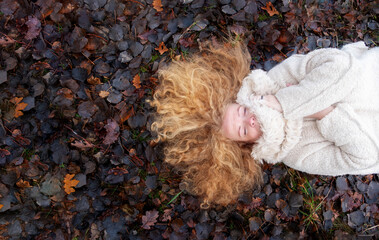 top view portrait of a beautiful sexy lovely mature redhead woman with long red curly hair lying on meadow covered with dark autumn leaves, copy space