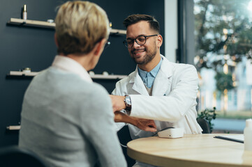 Young smiling doctor checking senior woman patient blood pressure
