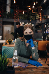Young restaurant workers waiters cleaning and disinfecting tables and surfaces against Coronavirus pandemic disease. They are wearing protective face masks and gloves.