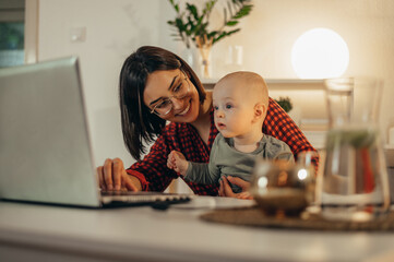 Beautiful business mom using a laptop and spending time with her baby boy at home