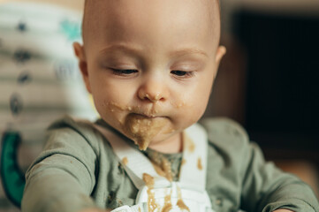 Baby eating with a face stained in food while in a child's dining chair