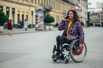 Obraz premium Woman in wheelchair using a smartphone while out in the city