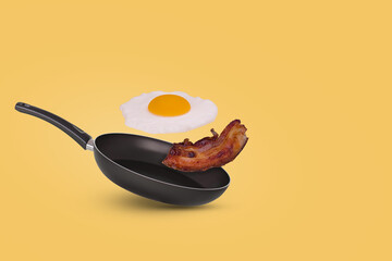 Minimal idea with a frying pan and a flying fried egg and bacon on a yellow background. Creative...