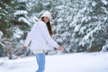 Close up portrait of happy girl in jacket  enjoying winter moments. Outdoors photo of a long-haired laughing lady in a knitted hat having fun on a snowy morning on a blurred background of wood