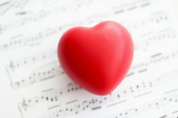 Red toy heart lying on paper with notes closeup
