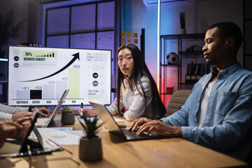 Four multiracial financial experts sitting at office with various gadgets and analysing financial growth in worldwide economy. Focus on Asian young lady posing on camera