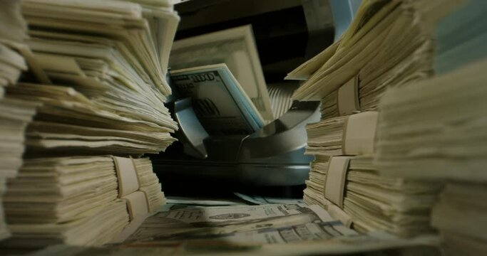 Close up shot of packs of US dollar bills lying around with cash counting machine working on background. Cash flow, business and financing 4k footage