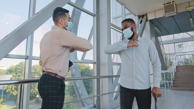Two multiracial colleagues multiethnic co-workers meet in office wearing protective medical masks. Afro american man safe handshake greeting during coronavirus outbreak elbow bump greet hello gesture