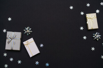 Fototapeta na wymiar Silver gift boxes. Gift box with gold ribbon, new year's decor and snowflakes in a christmas composition on a black background for a greeting card. Decoration and copy space for your text.