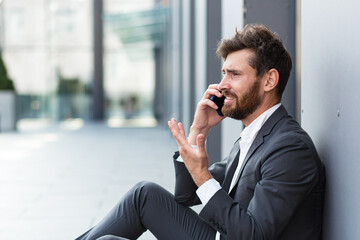 Businessman in despair reports bad news talking on the phone, depressed and sad, sitting at the office lost hope
