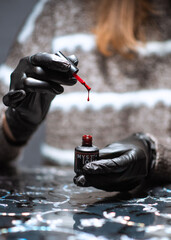 hands in black gloves hold gel polish from the brush of which a red drop is dripping, filmed with...