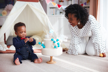 cute baby boy with his first birthday cake at home with mother