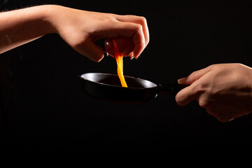 Breaking egg with one hand, isolated on black background. Pouring egg on frying pan for frying. Egg dropping. Advertising concept for cooking.