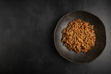 Ground beef in dark plate on the table.