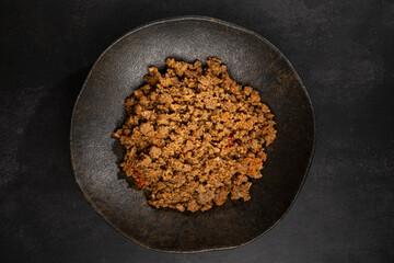 Ground beef in dark plate on the table.