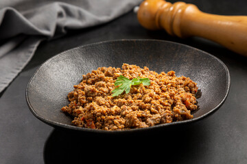 Ground beef in dark plate on the table.