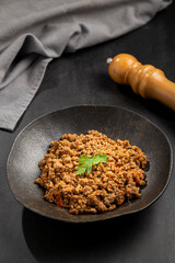 Ground beef in dark plate on the table.