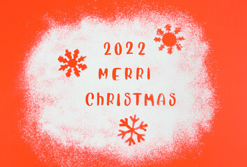 Stencil of number 2022 with the inscription: Merry Christmas and three snowflakes in white flour on a red.