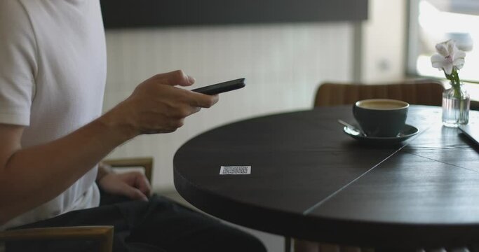 Close-up of smartphone in male hands tapping on screen. Man scanning QR code on table in restaurant or cafe. Online menu for clients. Convenience, contactless concept.