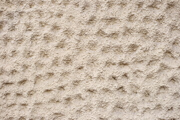 Beige facade plaster with scratches and indentations, close-up. Beige scratched stucco background