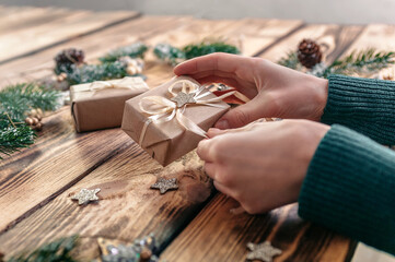 Women's hands are wrapping gifts on the background of a wooden table with gifts, fir branches and items for creativity
